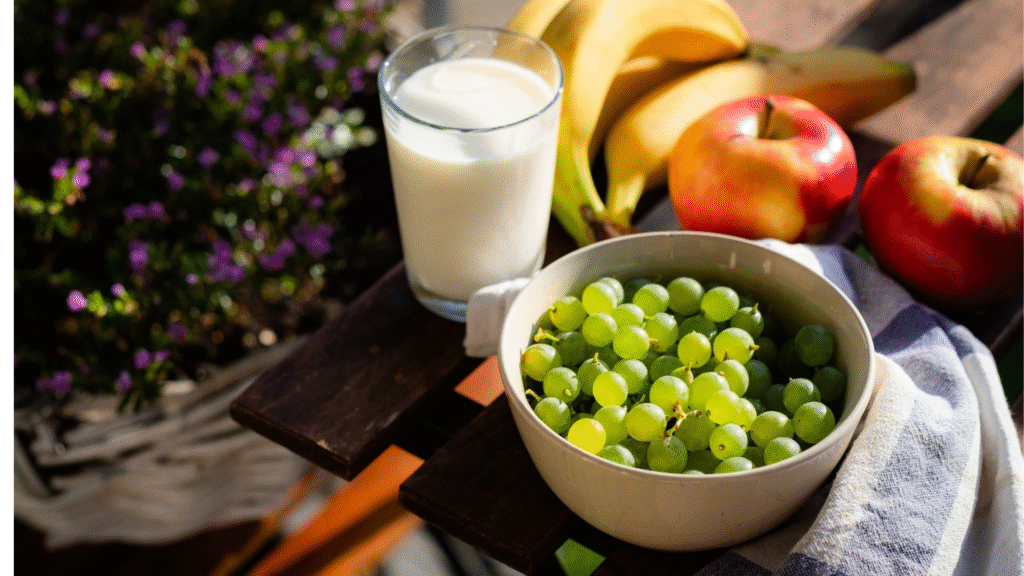 Healthy breakfast with fresh fruits, grapes, apples, bananas, and a glass of milk on a wooden table, supporting balanced diet and nutrition.